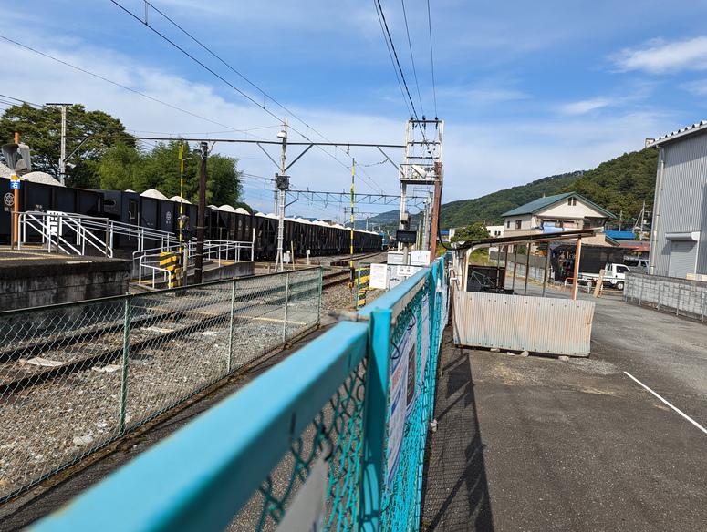 和銅黒谷駅の踏切と砂利を積んだ貨物列車